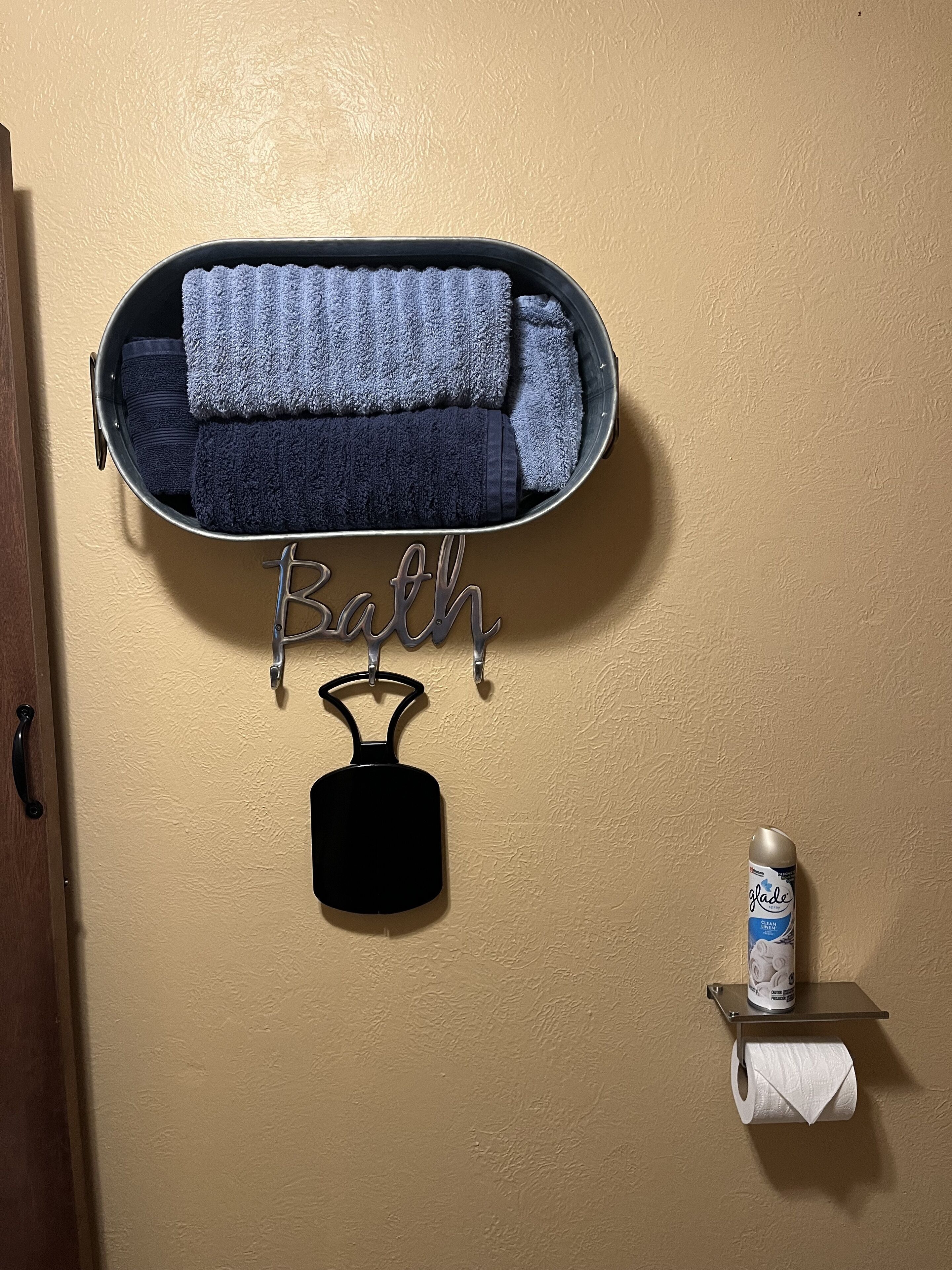 A bathroom with a towel rack holding folded towels, a black soap dish, and a toilet paper holder with a roll.