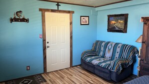 A room with a wooden floor, a white door, a blue wall, a patterned sofa, a framed picture, and a wooden cabinet. - Casita with Mountain View (Congress)