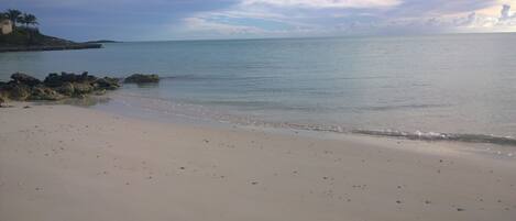 A beach with a calm sea, a sandy shore, and a rocky outcrop with vegetation.