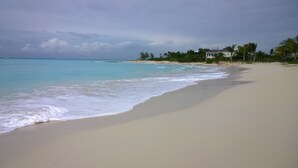 A beach with a sandy shore, calm waves, and a few buildings in the background.