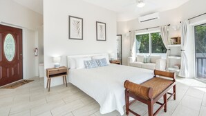 A spacious bedroom with a large bed, a wooden bench, a sofa, and a view of the outdoors.