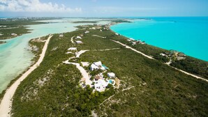 An aerial view of a coastal property with multiple buildings, a beach, and clear turquoise waters.