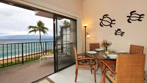 Een balkon met uitzicht op de oceaan, een eettafel met stoelen en decoratieve muurkunst.