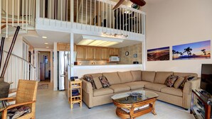 Een ruime woonkamer met een hoge plafond, een grote bank, een glazen salontafel en een televisie.