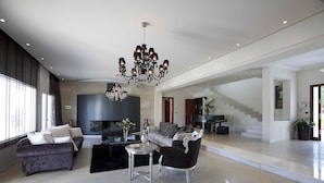 A spacious living area with a chandelier, a sofa set, a coffee table, and a staircase leading to another level. - Villa Elena Perea Thessaloniki (Perea Thessaloniki)