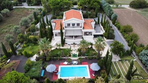 A large, white, two-story house with a red-tiled roof, surrounded by lush greenery and a swimming pool. - Villa Elena Perea Thessaloniki (Perea Thessaloniki)