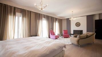 A bedroom with a large bed, two chairs, a sofa, a chandelier, and a fireplace.