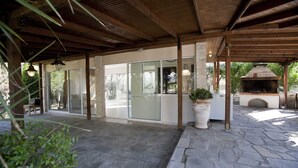 A covered patio area with stone flooring, a glass door entrance, and a brick oven. - Villa Elena Perea Thessaloniki (Perea Thessaloniki)