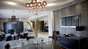 A modern dining area with a glass table, elegant chandelier, and a cityscape painting on the wall. - Villa Elena Perea Thessaloniki (Perea Thessaloniki)