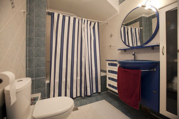 A bathroom with a striped shower curtain, a white toilet, a blue sink, and a red towel. - Villa Elena Perea Thessaloniki (Perea Thessaloniki)