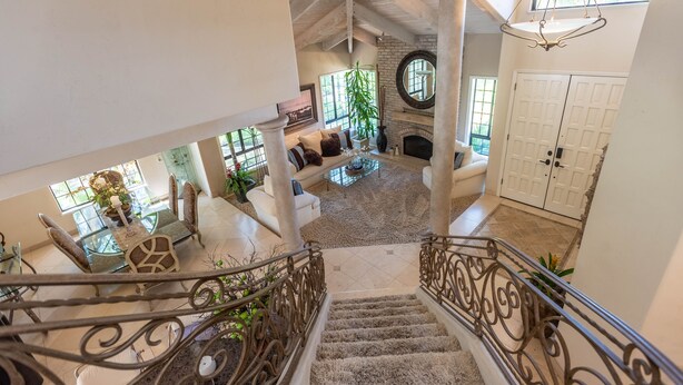 A spacious living area with a high ceiling, a fireplace, and a staircase with ornate railings. - A Writer's Hideaway and Private Escape for the Hollywood Elite. (Westlake Village)