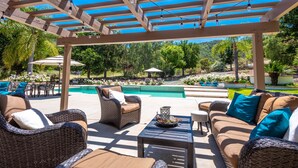 A covered outdoor seating area with wicker furniture, a pool, and a pergola with string lights. - A Writer's Hideaway and Private Escape for the Hollywood Elite. (Westlake Village)