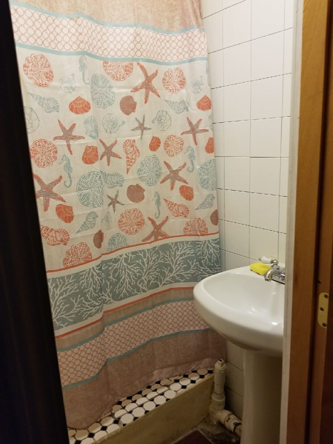 A bathroom with a shower curtain featuring a sea-themed pattern, a white sink, and a tiled floor.
