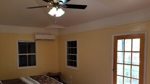 Une chambre à coucher avec un lit, deux fenêtres, un ventilateur de plafond et une porte.