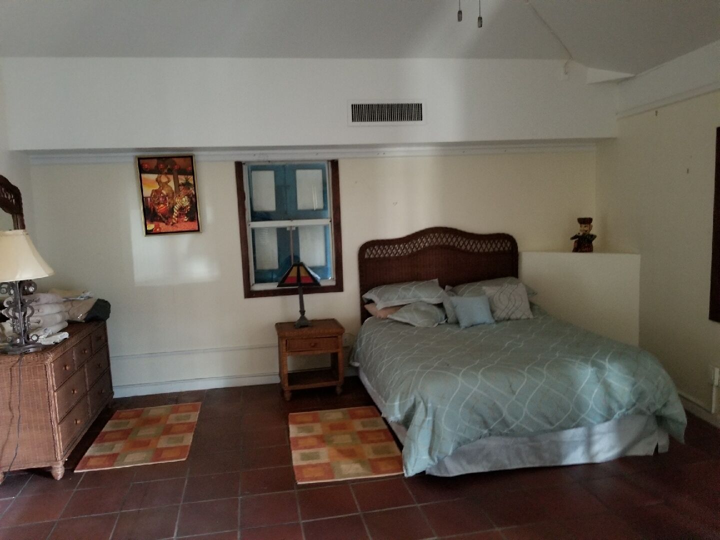 A bedroom with a bed, a nightstand, a dresser, a window, and a wall-mounted vent.
