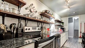 A modern kitchen with stainless steel appliances, wooden shelves, and a tiled backsplash. - Indie Escape-2 in 1- stone’s throw to the Plaza (Oklahoma City)