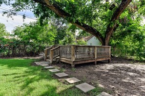 Eine Holzterrasse mit einer Treppe, die zu einer Bank führt, umgeben von Bäumen und einer Rasenfläche.