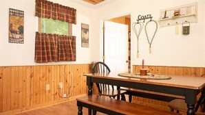A wooden-paneled room with a dining table, bench, and a coat rack with whisks. - Quaint cottage in the Smoky Mountain area convenient to all the attractions (Kodak)