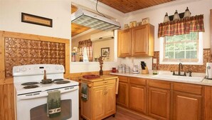 A kitchen with wooden cabinets, a white stove, and a window with a plaid valance. - Quaint cottage in the Smoky Mountain area convenient to all the attractions (Kodak)