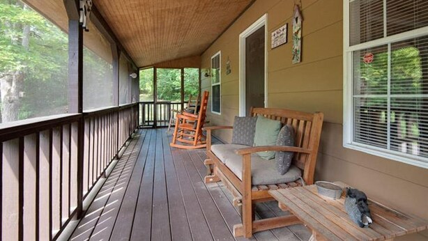 A wooden porch with a bench and chairs, a small table, and a window with blinds. - Quaint cottage in the Smoky Mountain area convenient to all the attractions (Kodak)
