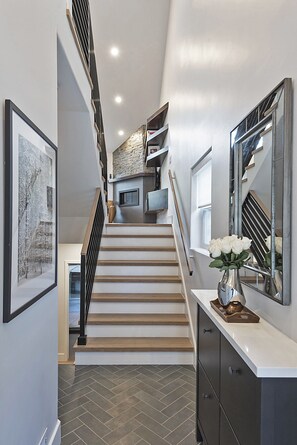 A modern staircase with wooden steps and a metal railing, leading to a landing with a stone wall and a television. - Perfect Location! Walk To Main St, Deer Valley Snow Park Base Lodge (Park City)