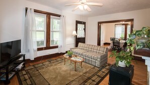 A living room with a television, a ceiling fan, a sofa, and a dining area with chairs and a table. - Charming Cottage in town~on Appalachian Trail~Mountain Views~   (Hot Springs)