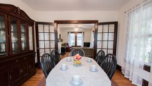 A dining room with a long table set for six, surrounded by chairs, with a wooden cabinet to the left and a window with curtains to the right. - Charming Cottage in town~on Appalachian Trail~Mountain Views~   (Hot Springs)