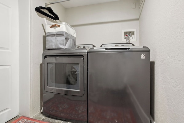 A compact, stainless steel laundry machine with a front-loading door, a small control panel, and a drying rack on top.
