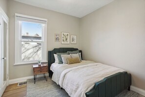 A bedroom with a bed, a nightstand, a window, and wall art.