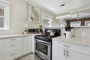 A modern kitchen with white cabinetry, a gas stove, a microwave, and a decorative piece on the wall.