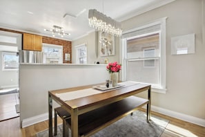 A modern kitchen with a wooden table, a vase of flowers, and a hanging light fixture.