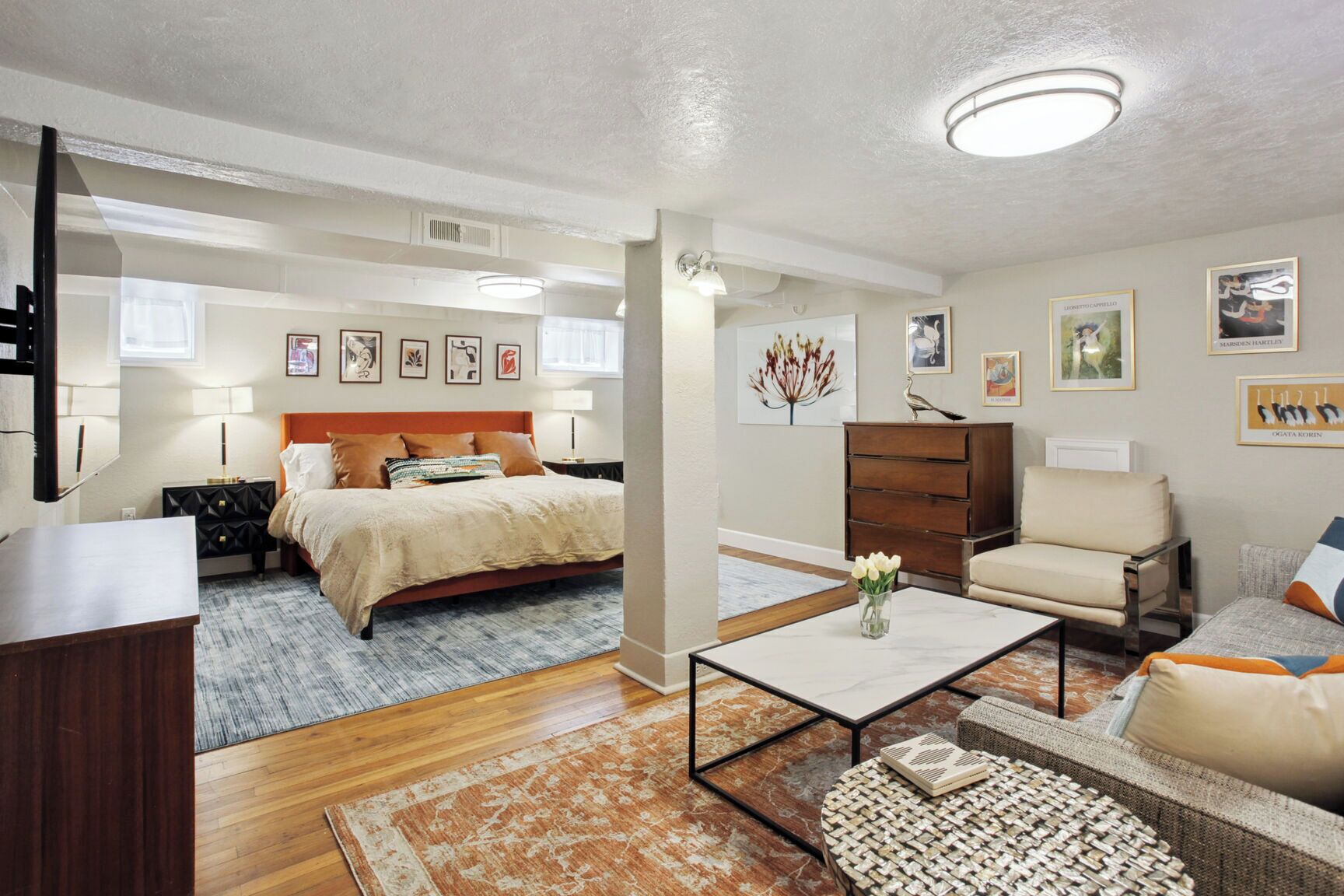 Un dormitorio bien iluminado con cama, mesitas de noche, cómoda y mesita auxiliar. Cuenta con una sala de estar con sofá, mesa de centro y sillón.