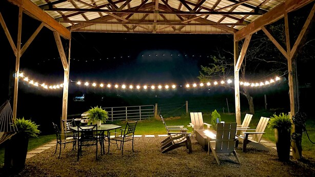 An outdoor covered patio with string lights, wooden chairs, a table, and potted plants. - Modern Farmhouse near VMI, W&L, SVU & VA Horse Ctr (Lexington)