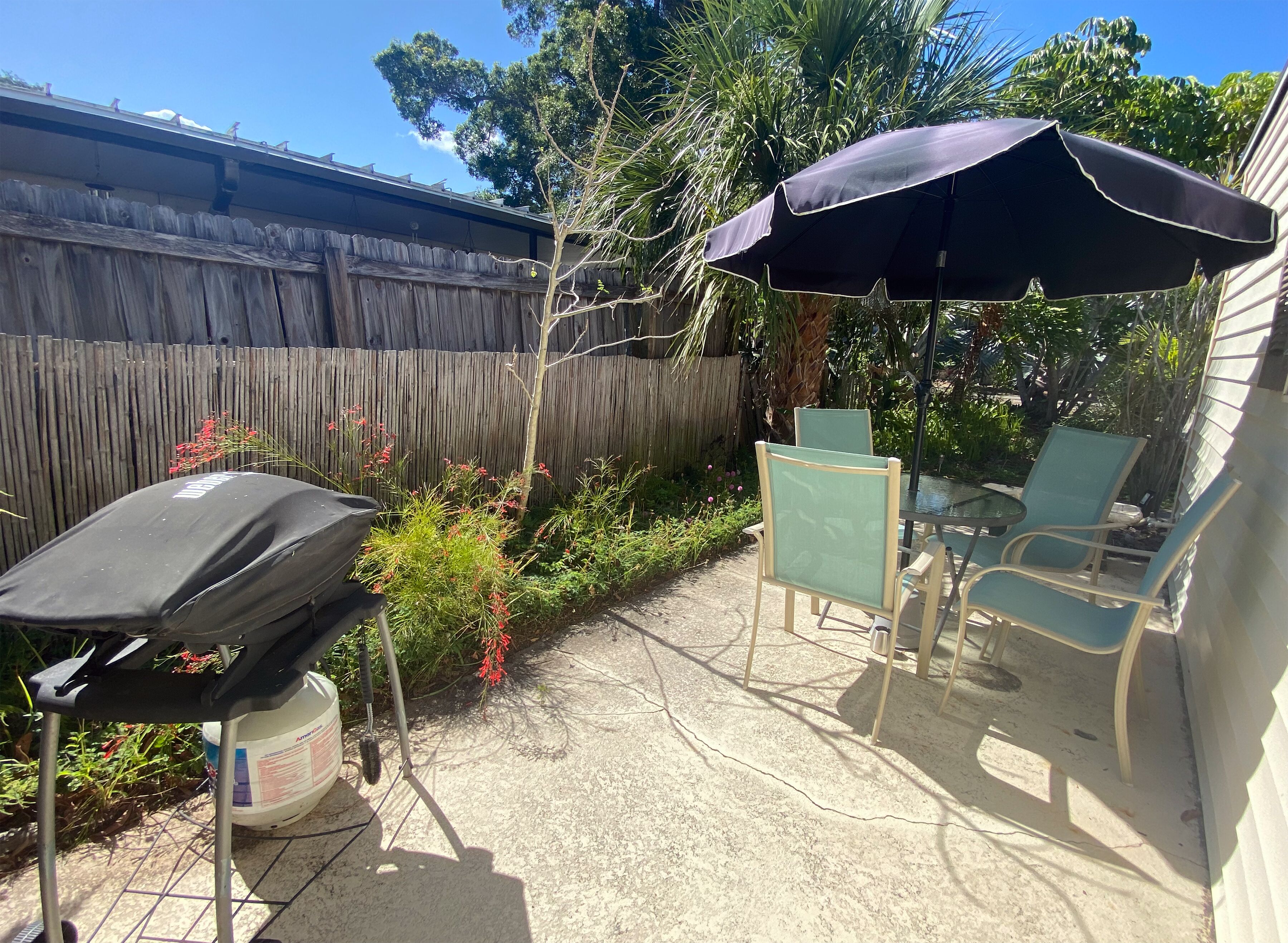 Un patio con zona de barbacoa cubierta, sillas exteriores y una mesa.