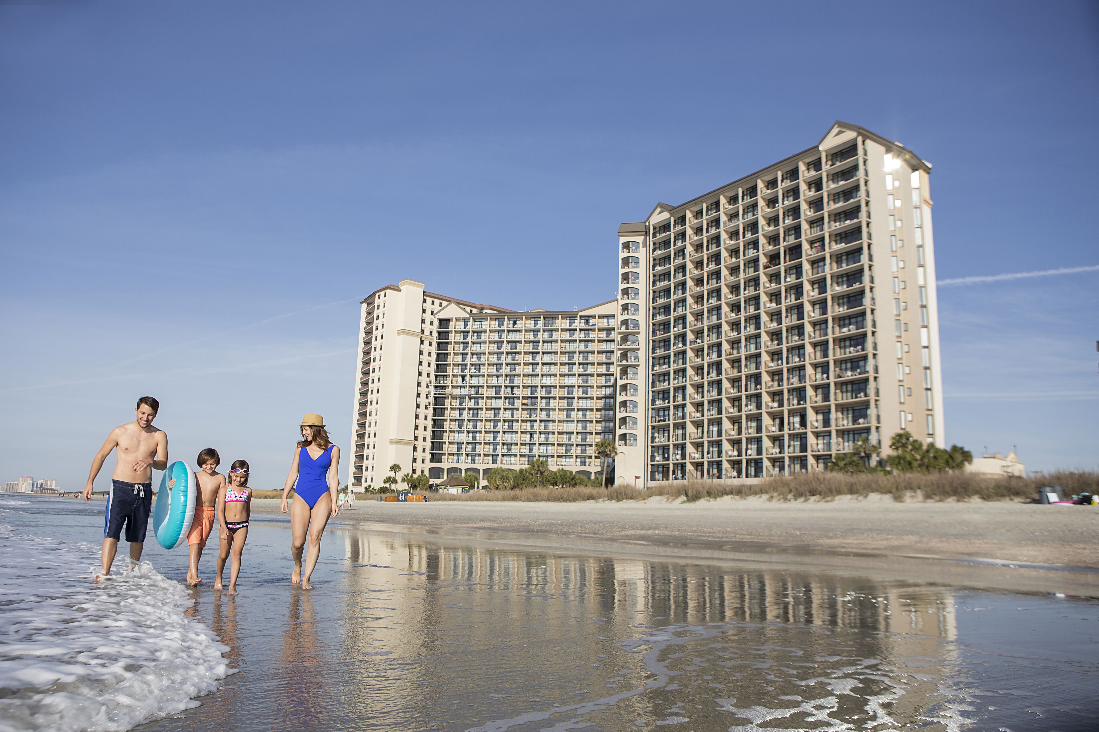 A beachfront hotel with multiple balconies, a sandy beach, and a clear sky.