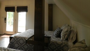 A bedroom with a sloped ceiling, a wooden beam, a bed with patterned bedding, and a door leading to a balcony. - Fish Eagle Loft ~ On the Lake ~ Beautiful Views~Great Fishing~Wildlife Abounds (Guntersville)