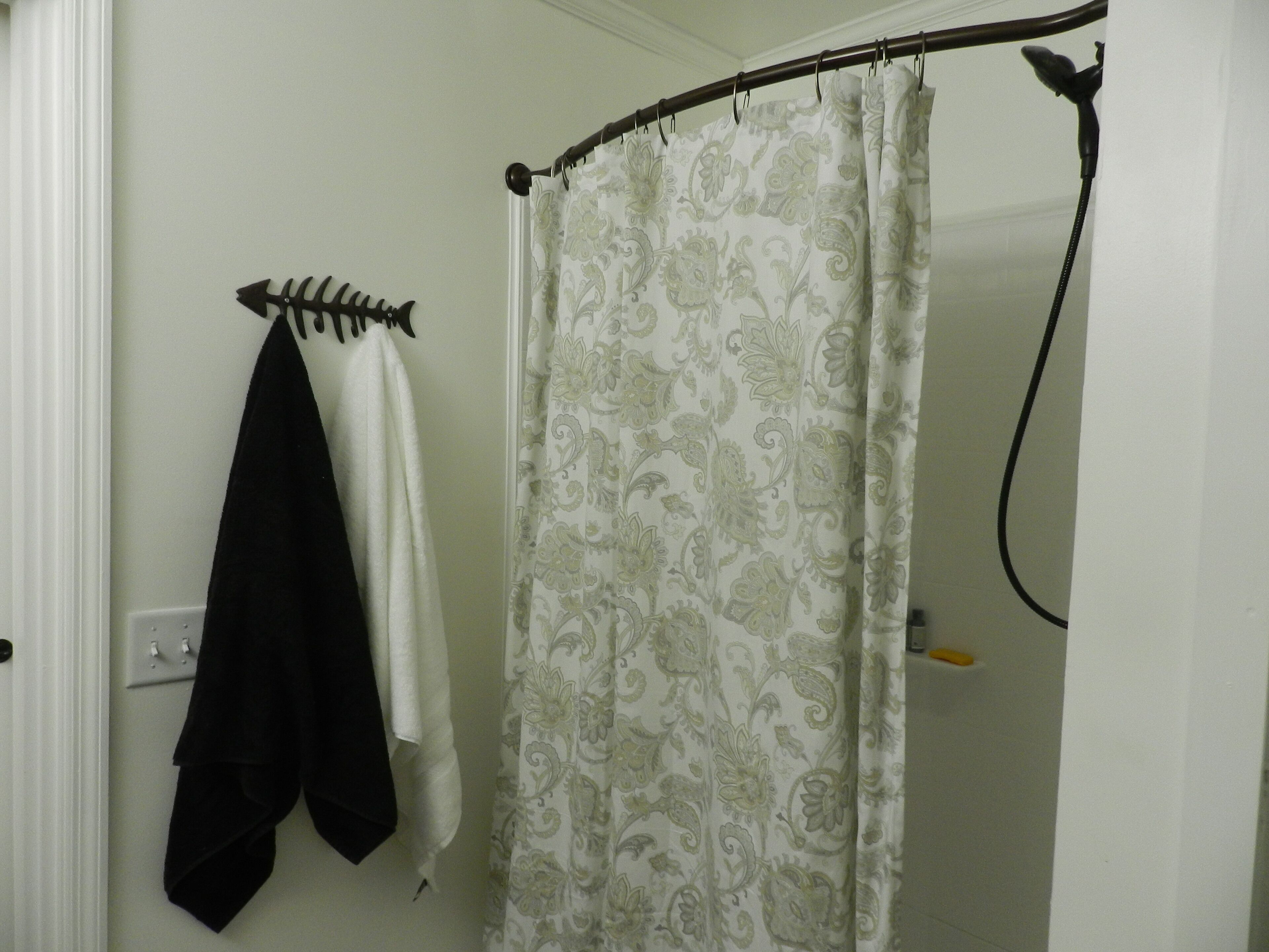 A bathroom with a shower curtain, a towel rack with towels, and a shower head.
