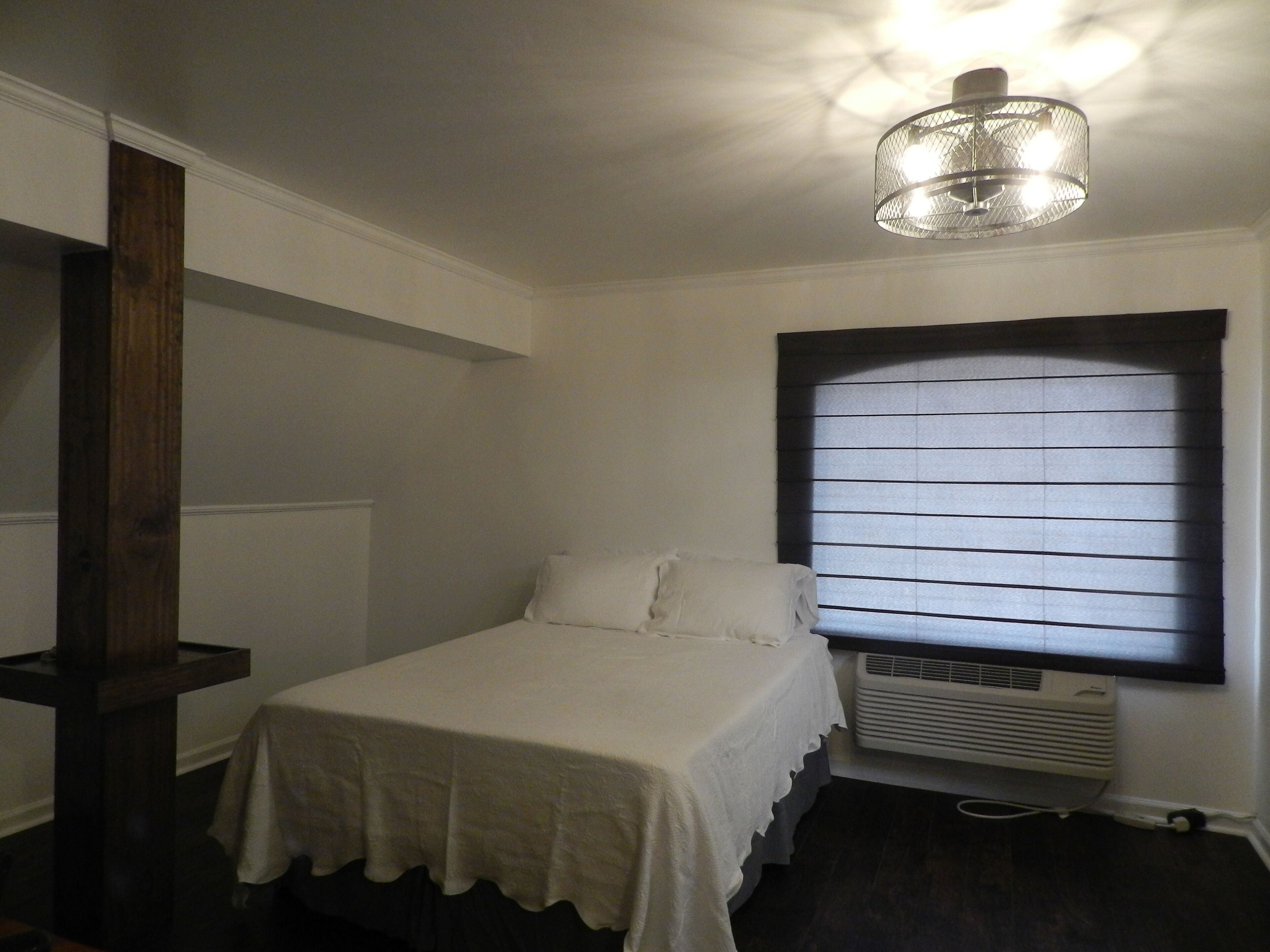 Ein Schlafzimmer mit einem Bett, einem Fenster mit Jalousien, einem Heizkörper und einer Deckenleuchte.