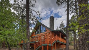 A log cabin with a stone chimney, wooden deck, and a staircase leading to the main entrance.
