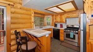 A wooden cabin-style kitchen with a central island, a stove, and a refrigerator.