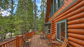 A log cabin with a wooden deck, outdoor seating, and a view of surrounding trees.