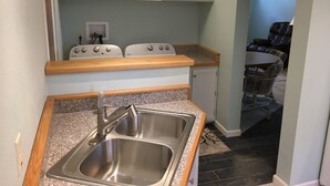 Cocina compacta con un lavamanos de acero inoxidable, dos estufas Whirlpool a gas blancas y un mueble pequeño.