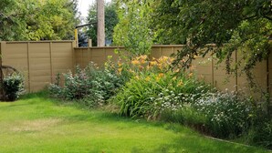 Un jardín con diversas plantas y flores, una valla de madera y una estructura metálica.