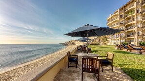 A beachside patio with a table and chairs, a large umbrella, and lounge chairs. - Costa Azul Oceanfront Condo w/Views, Surf, Swimmable Beach (San Jose del Cabo)