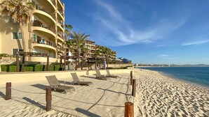 A beachfront hotel with multiple balconies, sun loungers, and a sandy beach. - Costa Azul Oceanfront Condo w/Views, Surf, Swimmable Beach (San Jose del Cabo)