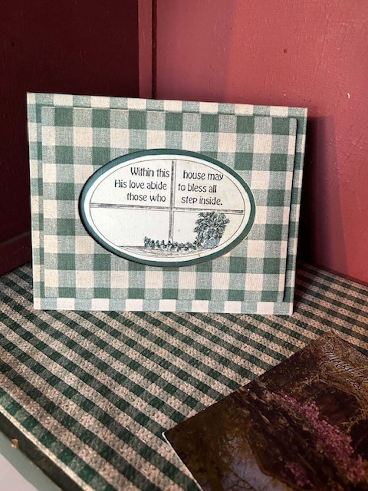 Una tarjeta con diseño de cuadros y un mensaje sobre amor y bendiciones, ubicada dentro de una casa.