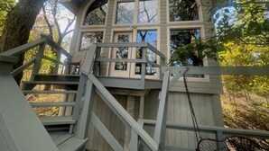 Una casa en árbol con fachada de madera, varias ventanas y una escalera que sube.