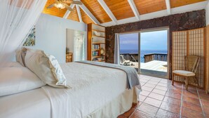 A bedroom with a large bed, a ceiling fan, a bookshelf, and a view of the ocean. - AS SEEN ON HGTV BEACH HUNTERS! Oceanfront, Amazing Whale Watching and Snorkeling (Captain Cook)