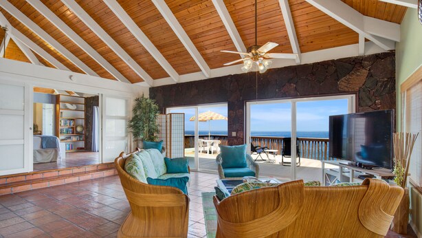 A spacious living area with a high ceiling, a large TV, wicker furniture, and a view of the ocean. - AS SEEN ON HGTV BEACH HUNTERS! Oceanfront, Amazing Whale Watching and Snorkeling (Captain Cook)