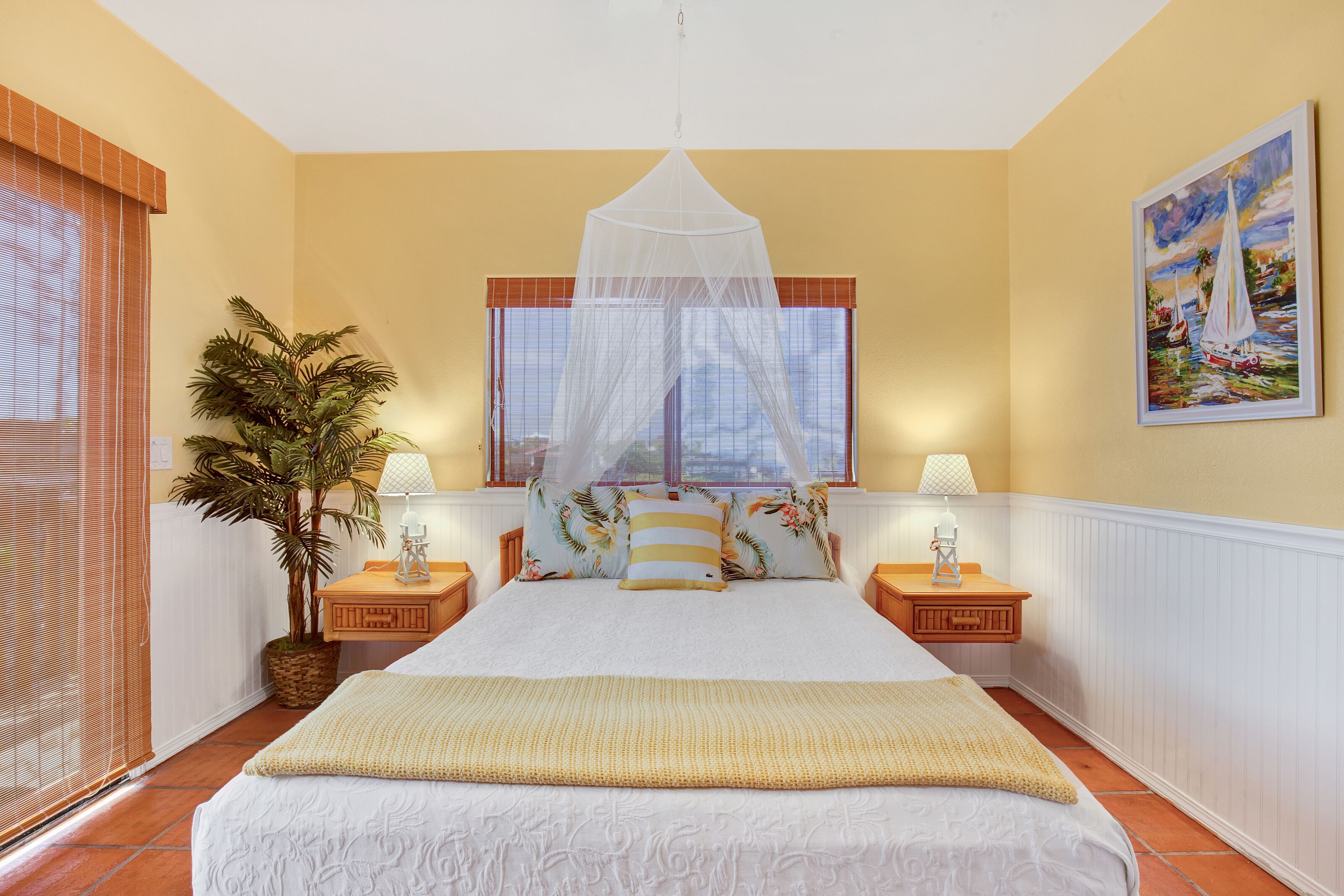 Ein Schlafzimmer mit Bett, Nachttisch, Lampe, Blumentopf und Fenster mit Vorhang.